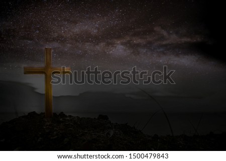 Cross wooden raised to the glory of God, Jesus Christ. Night light lighting a fire on a background of stones under the stars of the Milky Way.