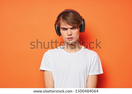 The guy in the headphones on an orange background is looking at the camera a cropped view                             