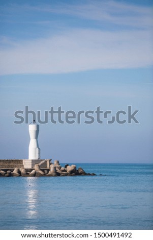 A modern white lighthouse is pictured against a blue sky, by the sea.
