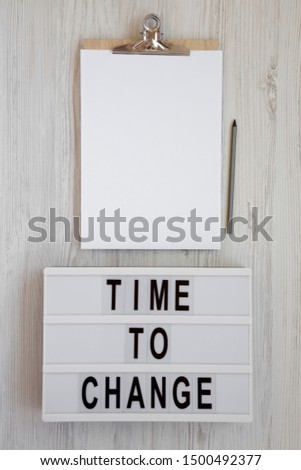 'Time to change' words on a modern board, clipboard with blank sheet of paper on a white wooden background, top view. Overhead, from above. Flat lay. Copy space.