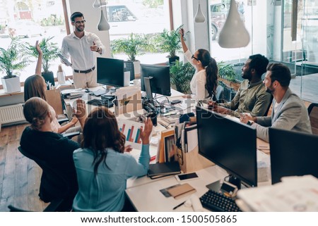 Group of young modern people in smart casual wear communicating and using modern technologies while working in the office Royalty-Free Stock Photo #1500505865