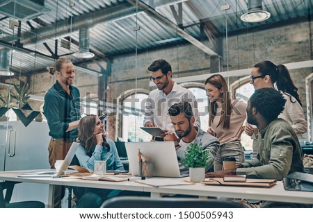 Group of young modern people in smart casual wear communicating and using modern technologies while working in the office                  Royalty-Free Stock Photo #1500505943