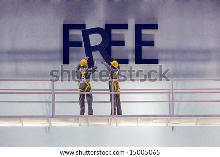 Workers preparing a billboard with the word "free" while standing on a scaffold.