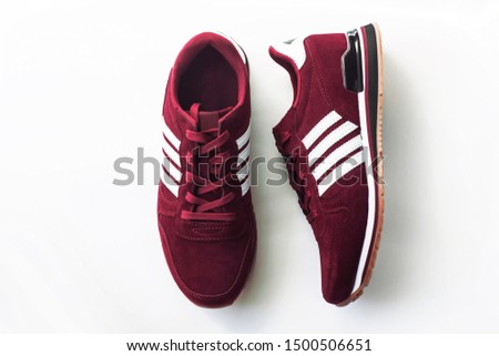 Burgundy sneakers on a white background with nature light shadows. Trendy sports shoes, active lifestyle. Copy space, top view, flatlay.