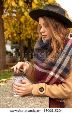Blonde pretty woman on a walk in european old city center. Cold autumn weather. Girl wears brown coat, plaid scarf and stylish hat