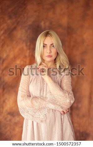 The girl gently raised her index dace to her face.Woman in a beige dress flirts with a camera squatting.Girl 30 old in a white lace dress.Fabric red background.For 30 years.Girl props up her chins