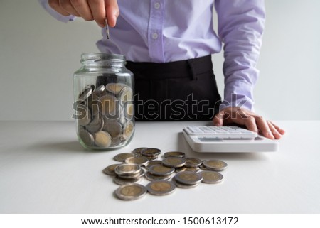 woman putting coin into Glass piggy bank with coins pile, step up growing business to success and saving for retirement  concept.