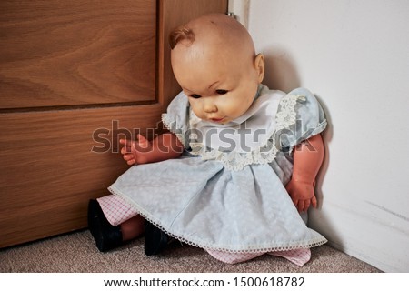 Old, worn and grimy toy doll with an eerie look, sitting in the corner of a room. Royalty-Free Stock Photo #1500618782