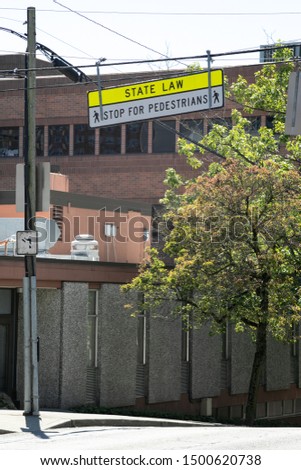 "State Law. Stop For Pedestrian" sign hanging above an urban intersection, with space for text on bottom