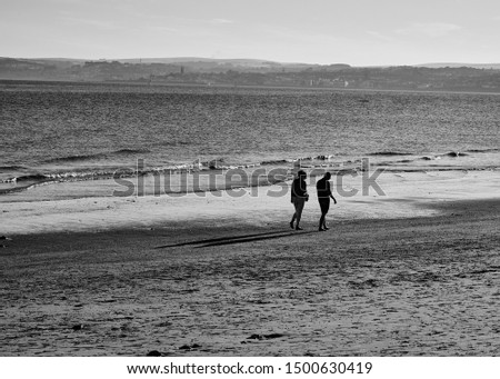 A loving couple contemplating their thoughts as they stroll across the beach at sunset.