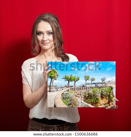 Photo canvas print. A smiling woman holding a rectangular photography with gallery wrap on red background. Landscape photo printed on glossy synthetic canvas and stretched on  stretcher bar