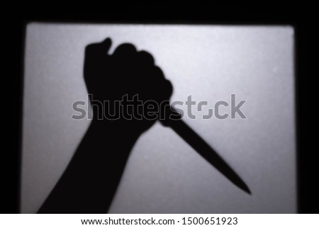 Blurred shadow of hand holding big sharp knife behind white mirror background. killer with knife.concept of scary crime scene of horror or thriller movies,Halloween theme