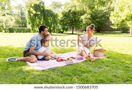 family, leisure and people concept - mother taking picture of happy father with two little sons by smartphone on picnic at summer park