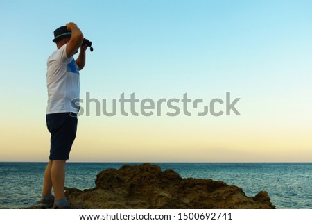 man looks through a telescope at the blue sea