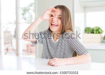 Beautiful young girl kid wearing stripes t-shirt doing ok gesture with hand smiling, eye looking through fingers with happy face.