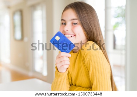 Beautiful young girl kid holding credit card with a happy face standing and smiling with a confident smile showing teeth