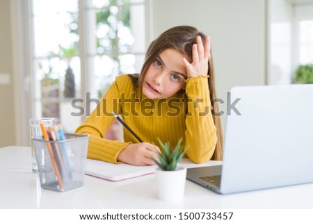 Beautiful young girl studying using computer laptop and writing on notebook stressed with hand on head, shocked with shame and surprise face, angry and frustrated. Fear and upset for mistake. Royalty-Free Stock Photo #1500733457
