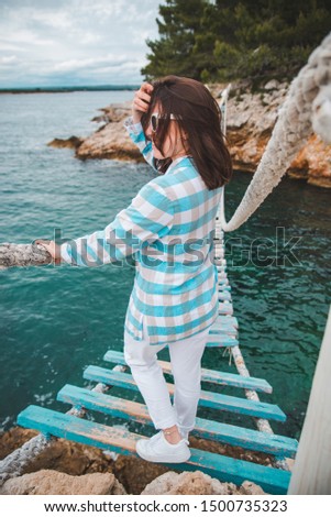 woman crossing suspension bridge sea on background summer time