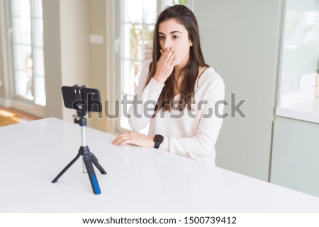 Beautiful young woman recording selfie video with smartphone webcam cover mouth with hand shocked with shame for mistake, expression of fear, scared in silence, secret concept