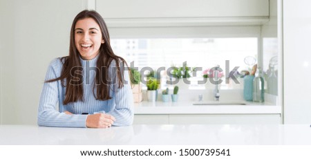 Wide angle picture of beautiful young woman sitting on white table at home with a happy and cool smile on face. Lucky person.