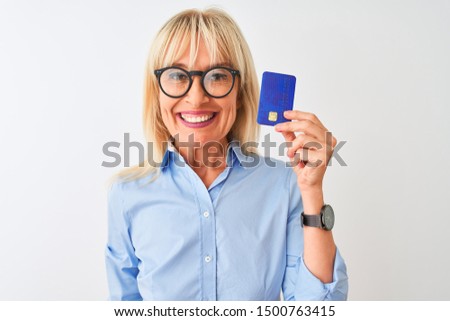 Middle age businesswoman wearing glasses holding credit card over isolated white background with a happy face standing and smiling with a confident smile showing teeth