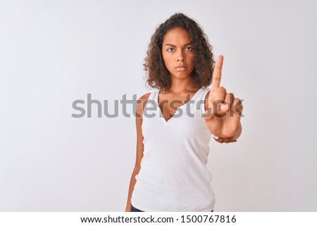 Young brazilian woman wearing casual t-shirt standing over isolated white background Pointing with finger up and angry expression, showing no gesture
