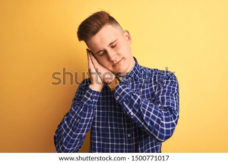 Young handsome man wearing casual shirt standing over isolated yellow background sleeping tired dreaming and posing with hands together while smiling with closed eyes.
