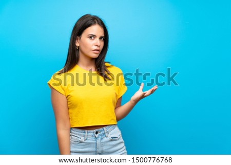 Young girl over isolated blue background making doubts gesture