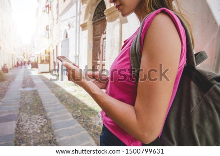 Close up cropped shot of female backpacker walking through old town street searching online city maps application on her mobile phone. Travel blogger making new post in social network.