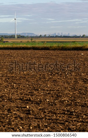 Close on a harvested potatoe field and a wind turbine in the vast farm land facing the Montreal skyine in Canada.