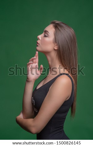 Profile view of young beautiful bwoman against green background.Young beautiful girl with brown hair in the studio on a green paper background. Modern girls. The girl gently touches her chin.