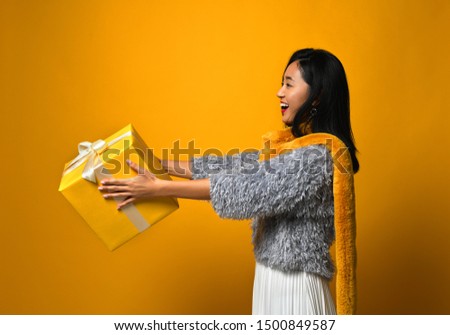 Portrait of a cute asian girl donates a gift box with joy, isolated over yellow background.