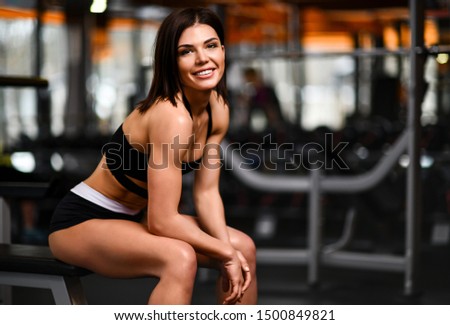 Young beautiful girl athlete sits resting after a difficult workout in the gym. Black orange picture. Live style