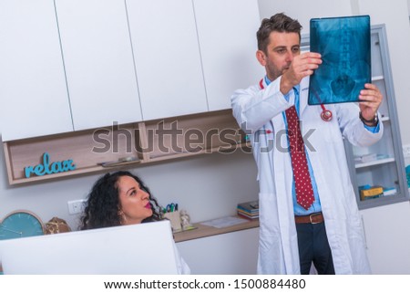 Male Doctor in his mid 40's reading an x-ray image (radiography) from a patient hip region (coxa) while standing in a hospital radiology department and discussing the result with a nurse.