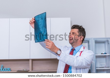 Male Doctor in his mid 40's reading an x-ray image (radiography) from a patient hip region (coxa) while standing in a hospital radiology department.