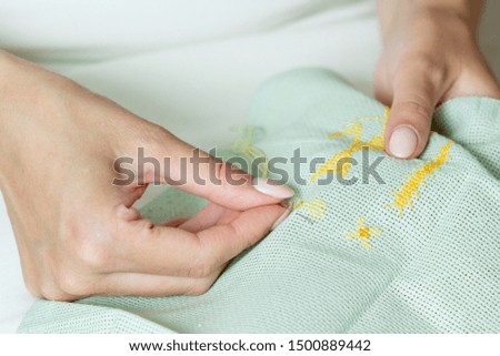 The process of cross-stitch on canvas. Girl's hands with embroidery.