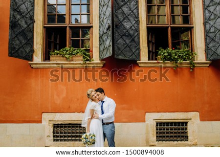 Sweet newlyweds standing under the windows of an orange building