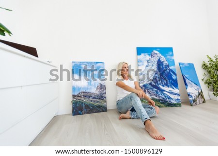 Happy blonde woman hanging large picture on wall at home