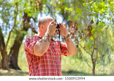 A male photographer holding a camera near his face and taking pictures on a camera in a park.