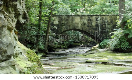 old stone bridge over a river with lush green landscape and large boulder rocks