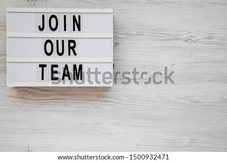 'Join our team' words on a modern board on a white wooden surface, top view. Overhead, from above, flat lay. Space for text.