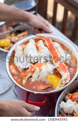 Hands lifting a stockpot of boiled crab claws and legs, in a seafood cookout scene