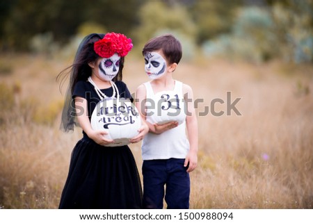 Asian Chinese girl and caucasian boy celebrating Halloween or carnival carrying white pumpkin. Sugar skull make-up or face paint. Outdoor portrait of child with costume and flower and veil on head.