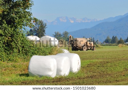 Summertime and farm production is in full swing as hay bales lay on a harvested land and a manure truck heads off in the background ready to fertilize the fields. 