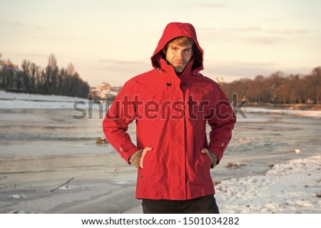 Hipster winter warm outfit. Guy wear jacket with hood on frosty winter day. Man bearded stand warm jacket snowy nature background. Wind resistant clothes. Winter menswear. Clothes for winter walks.