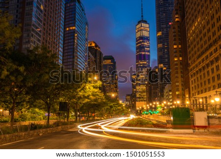 Downtown Manhattan street view at dawn featuring car lights on the foreground and buildings on the background