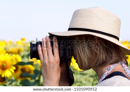 The photographer takes flowers of sunflower in the field. Fragment of a girl in a hat with a camera in profile taking pictures outdoors on a summer day. Side view, close-up, horizontal.