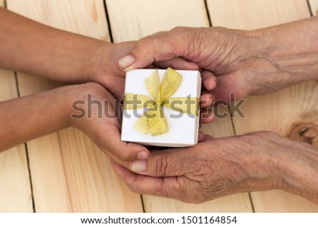 Hands of an elderly man and children's hands are holding a box with a gift. The concept of caring for old people, giving a gift for the holidays, birthday, Christmas. Image.