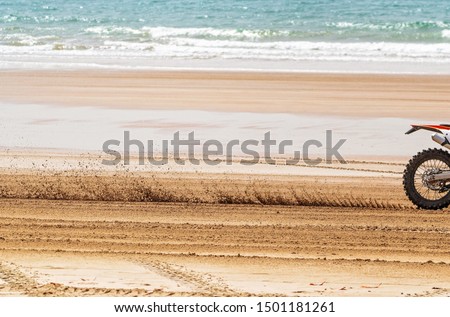 A close view of the blurred sand stirred up by a motorcyclist racing fast along the beach