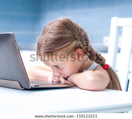 upset little girl with her computer at home at the table
